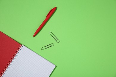 Photo of Notebook, paper clips and pen on light green background, top view. Space for text