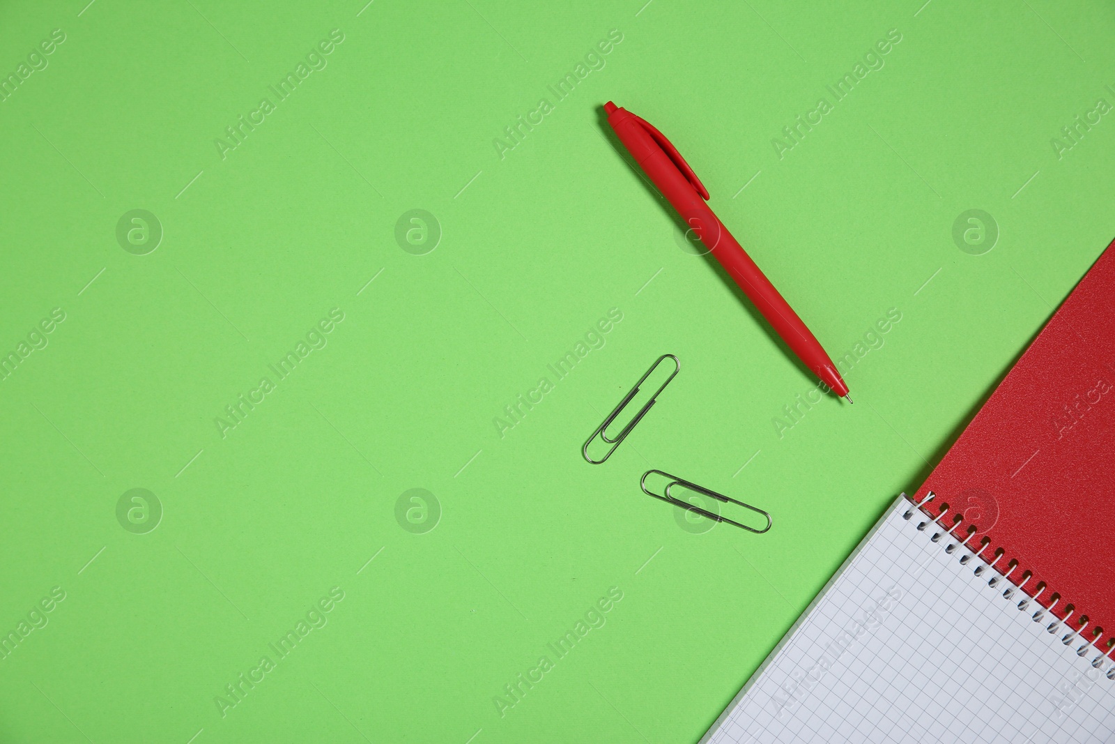 Photo of Notebook, paper clips and pen on light green background, top view. Space for text