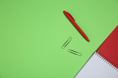 Photo of Notebook, paper clips and pen on light green background, top view. Space for text