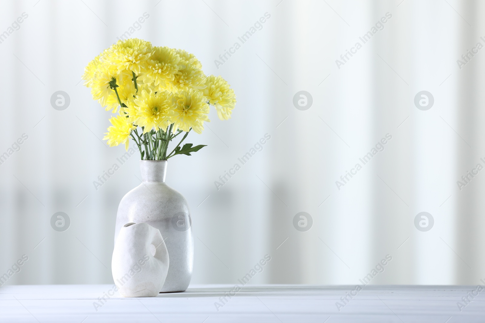 Photo of Beautiful yellow flowers in vase on white wooden table at home. Space for text