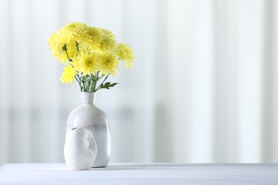 Photo of Beautiful yellow flowers in vase on white wooden table at home. Space for text