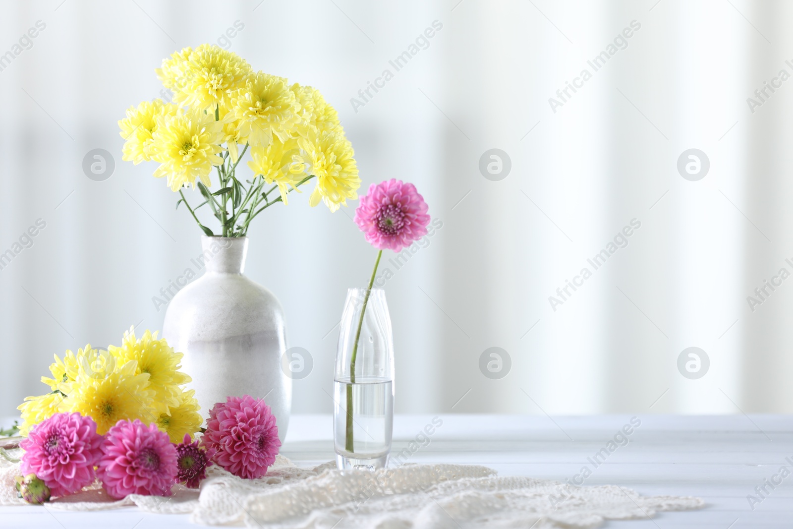 Beautiful yellow and pink flowers in vases on white wooden table at home. Space for text Photo of Beautiful yellow and pink flowers in vases on white wooden table at home. Space for text