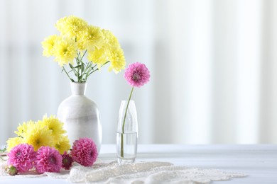 Photo of Beautiful yellow and pink flowers in vases on white wooden table at home. Space for text