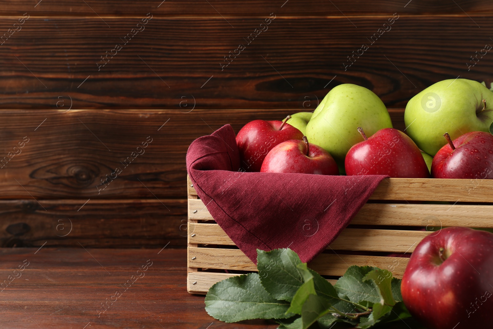 Photo of Ripe red and green apples in crate on wooden table, space for text