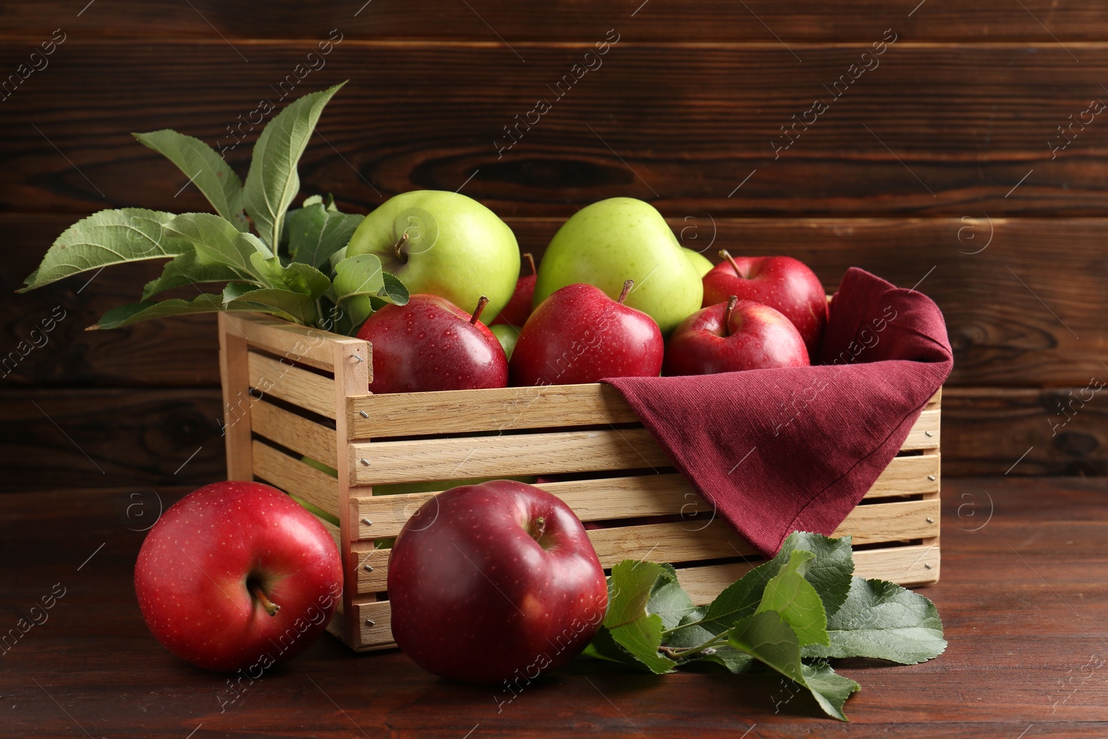 Ripe red and green apples in crate on wooden table Photo of Ripe red and green apples in crate on wooden table