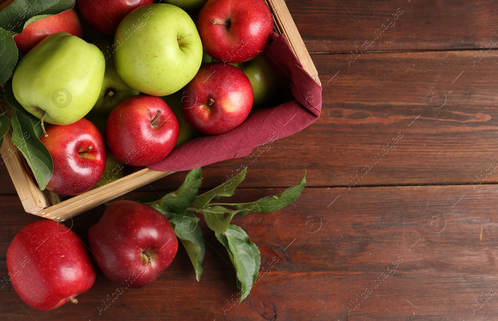 Photo of Ripe red and green apples in crate on wooden table, top view. Space for text