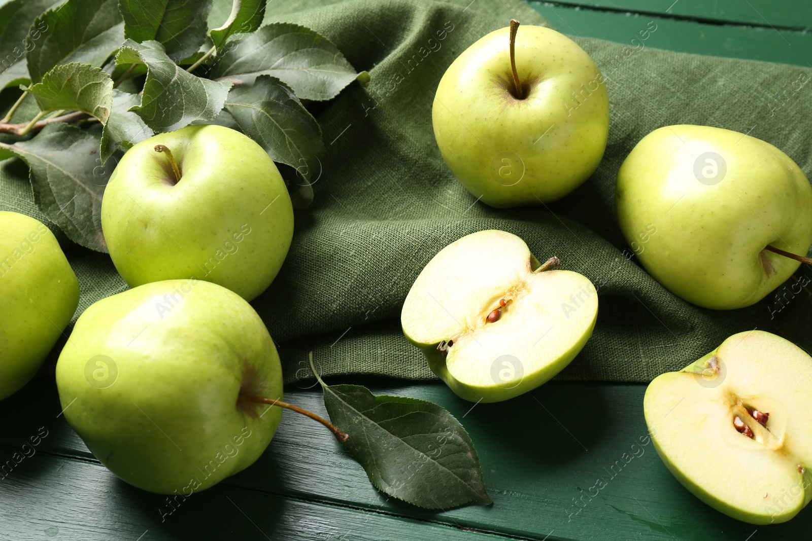 Photo of Ripe apples and leaves on green wooden table