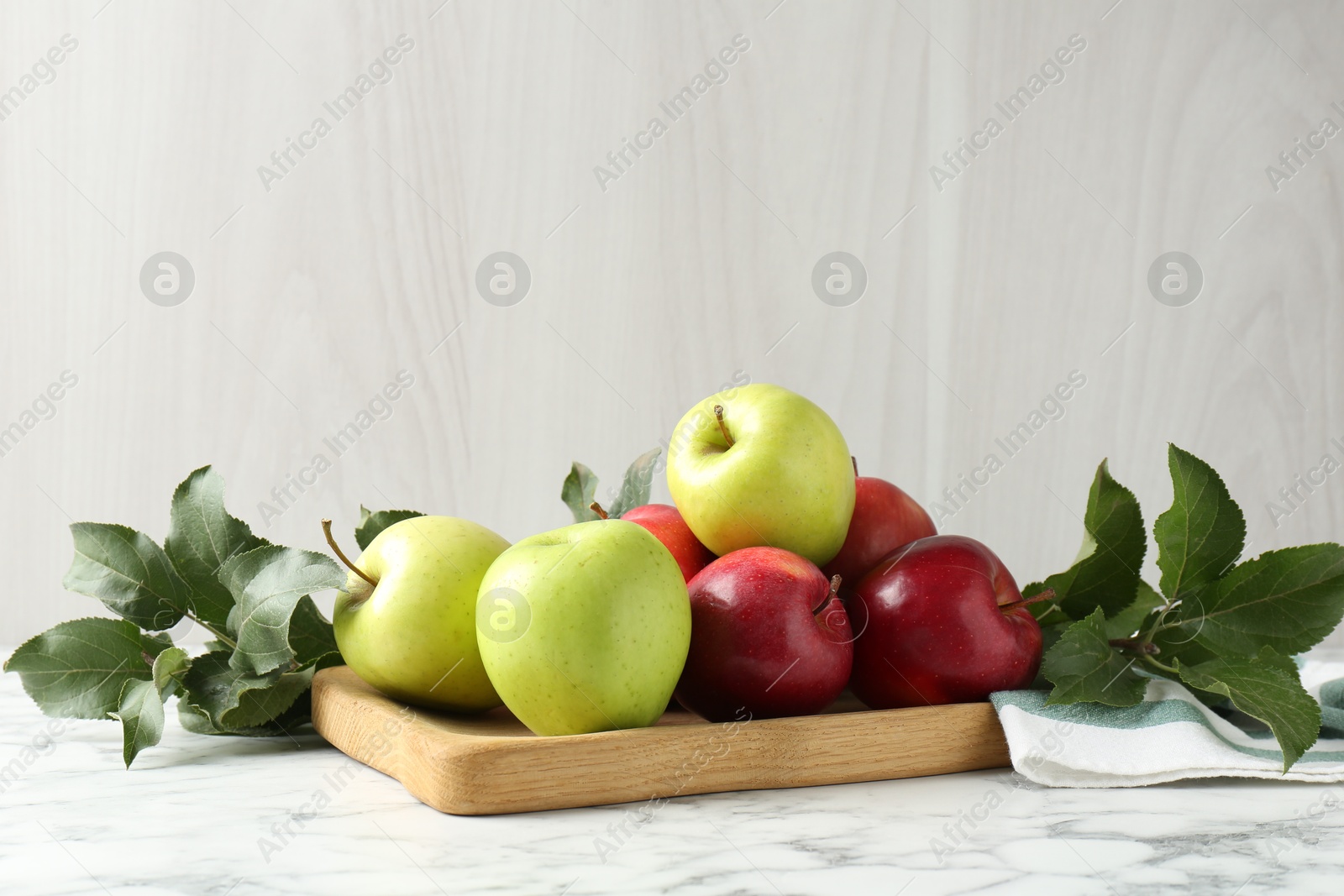 Photo of Ripe apples and green leaves on white marble table