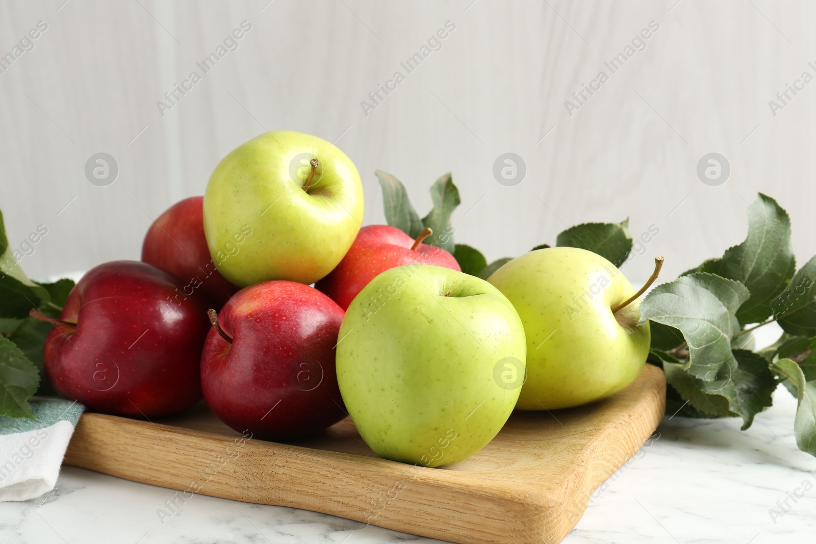 Photo of Ripe apples and green leaves on white marble table, closeup