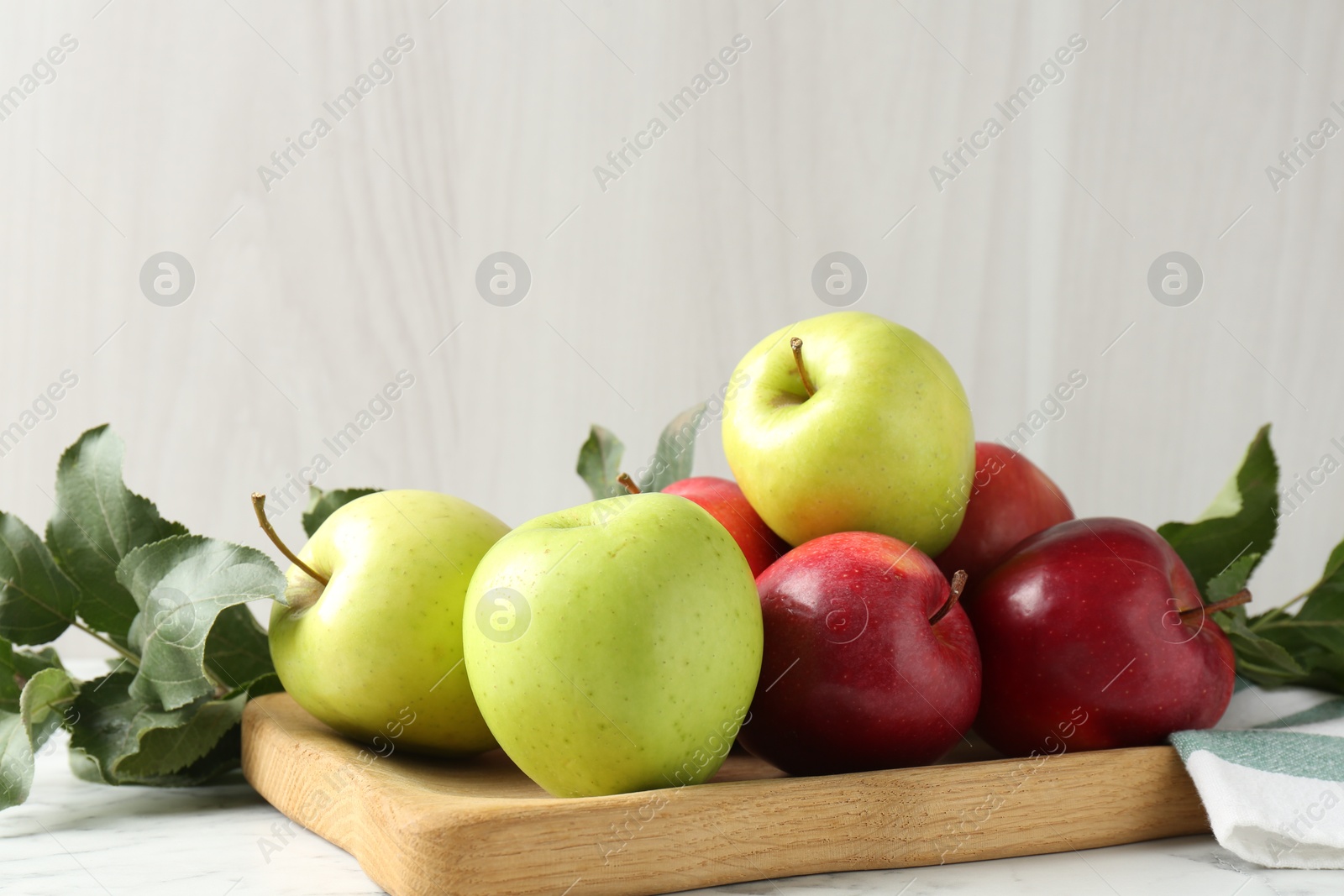 Photo of Ripe apples and green leaves on white marble table