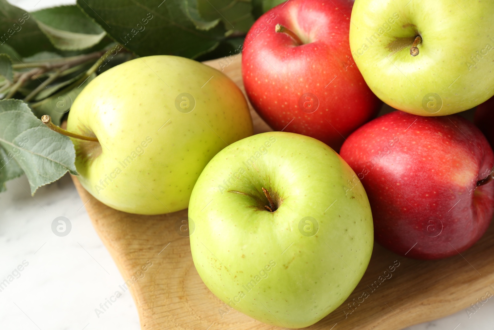 Photo of Ripe apples and green leaves on white table, closeup