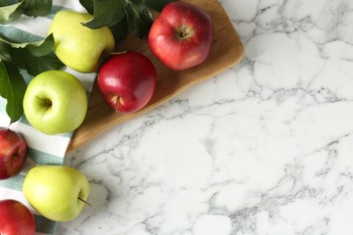 Photo of Ripe apples and green leaves on white marble table, top view. Space for text