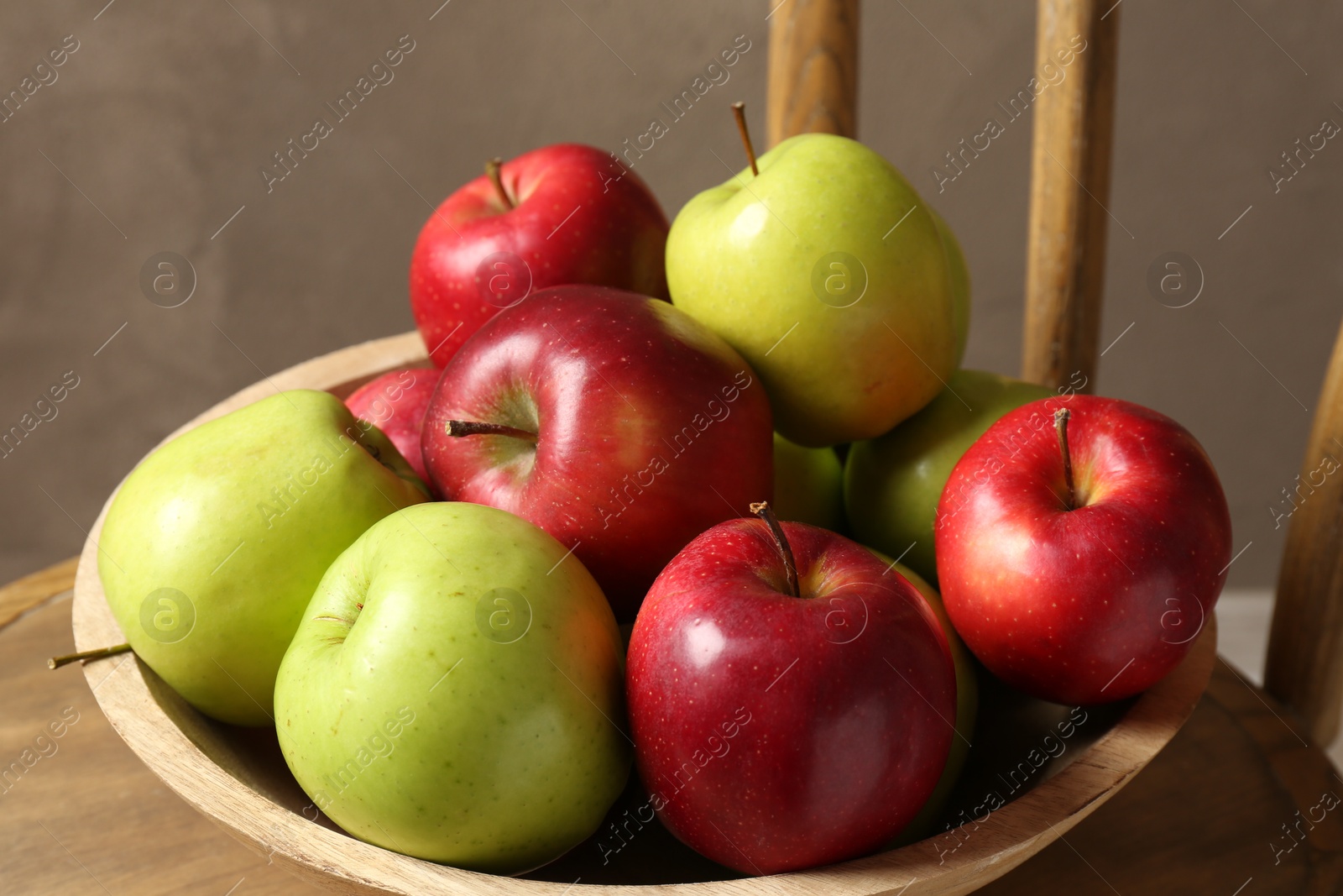 Photo of Ripe red and green apples in bowl on chair near grey wall, closeup