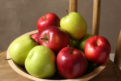 Photo of Ripe red and green apples in bowl on chair near grey wall, closeup