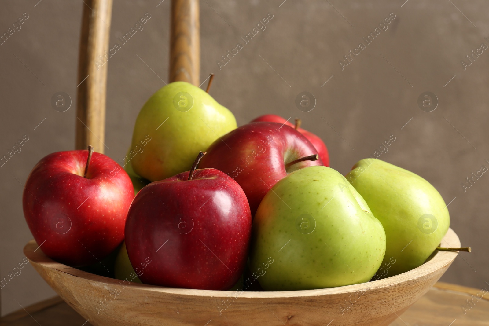 Photo of Ripe red and green apples in bowl on chair near grey wall, closeup