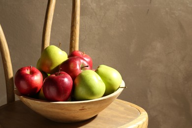 Photo of Ripe red and green apples in bowl on wooden chair near grey wall. Space for text