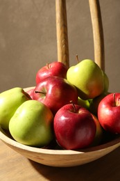 Photo of Ripe red and green apples in bowl on wooden chair near grey wall, closeup