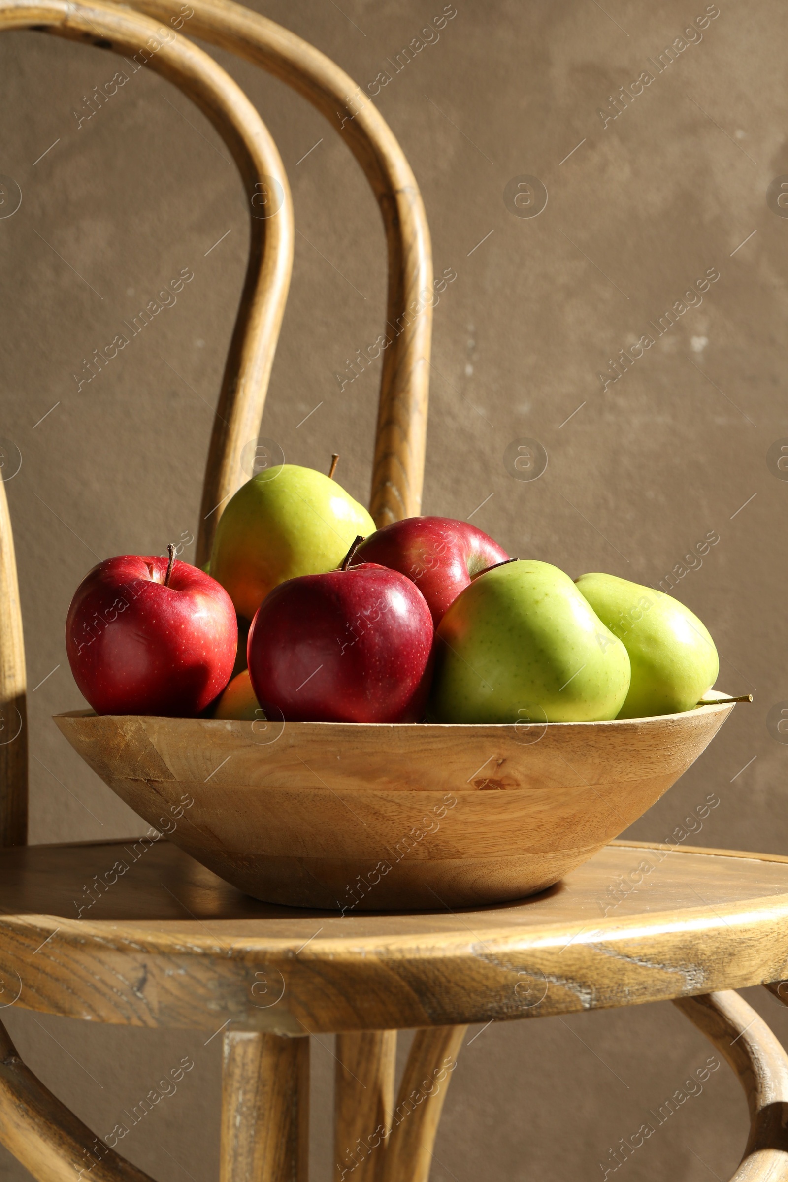 Photo of Ripe red and green apples in bowl on wooden chair near grey wall