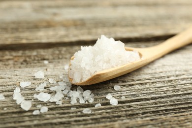 Photo of Sea salt in spoon on wooden table, closeup