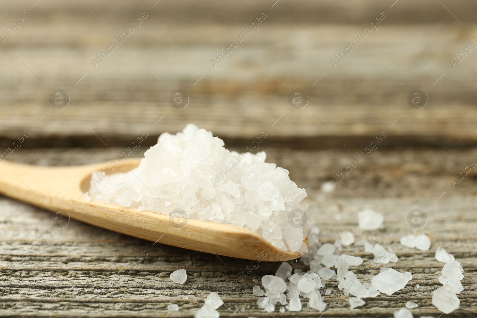 Photo of Sea salt in spoon on wooden table, closeup