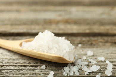 Sea salt in spoon on wooden table, closeup