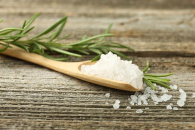 Photo of Sea salt in spoon and rosemary on wooden table, closeup