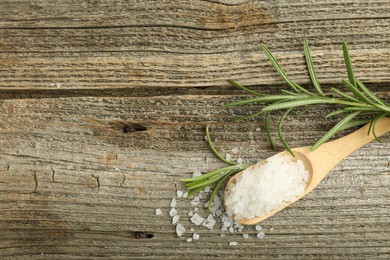 Sea salt in spoon and rosemary on wooden table, top view. Space for text