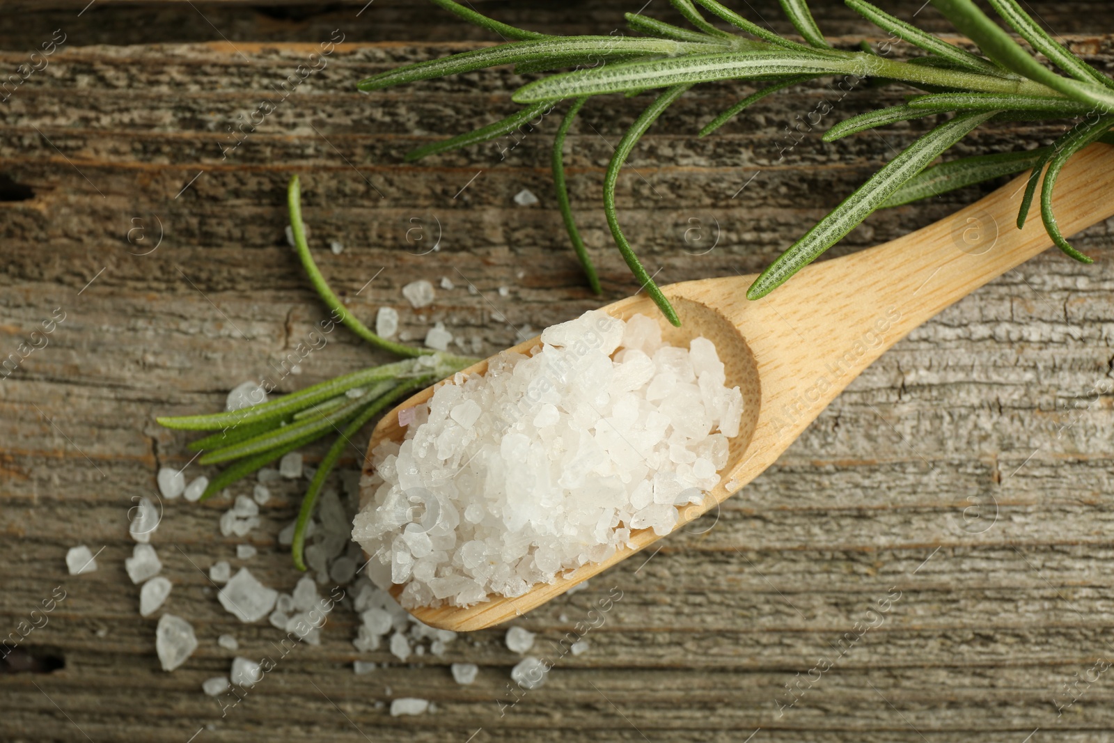 Photo of Sea salt in spoon and rosemary on wooden table, top view