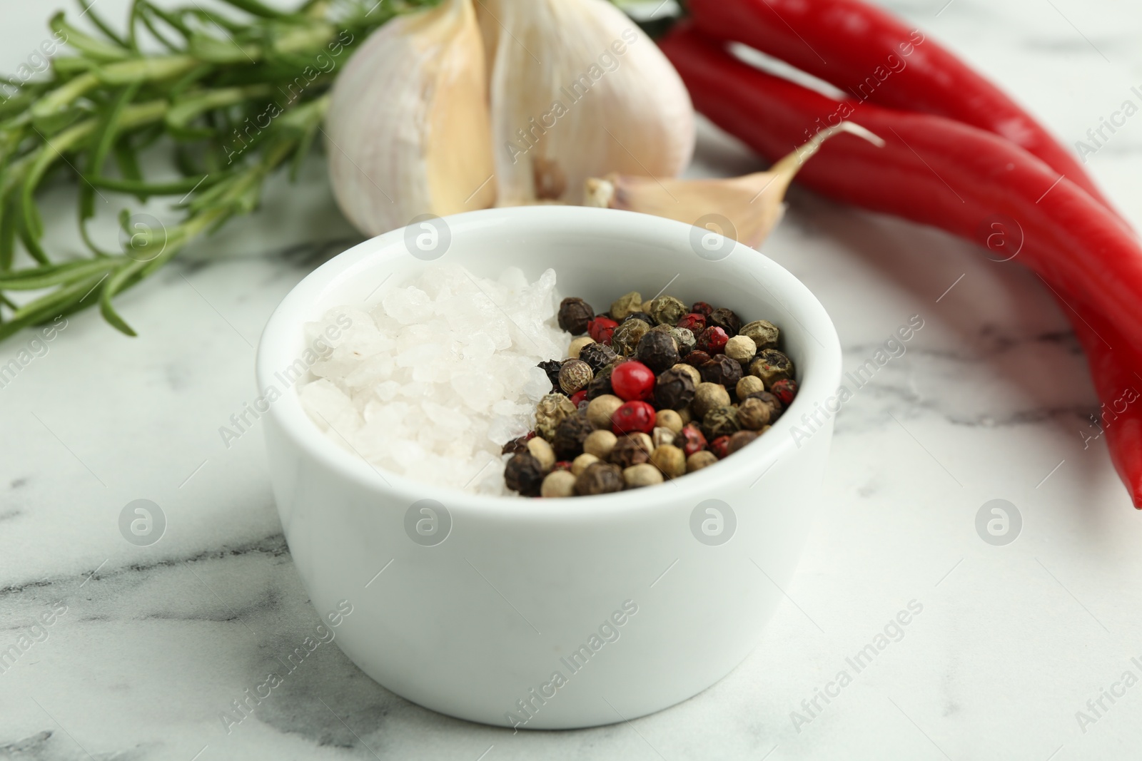 Photo of Sea salt, peppercorns, rosemary, chili peppers and garlic on white marble table, closeup