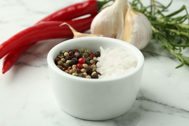 Photo of Sea salt, peppercorns, rosemary, chili peppers and garlic on white marble table, closeup