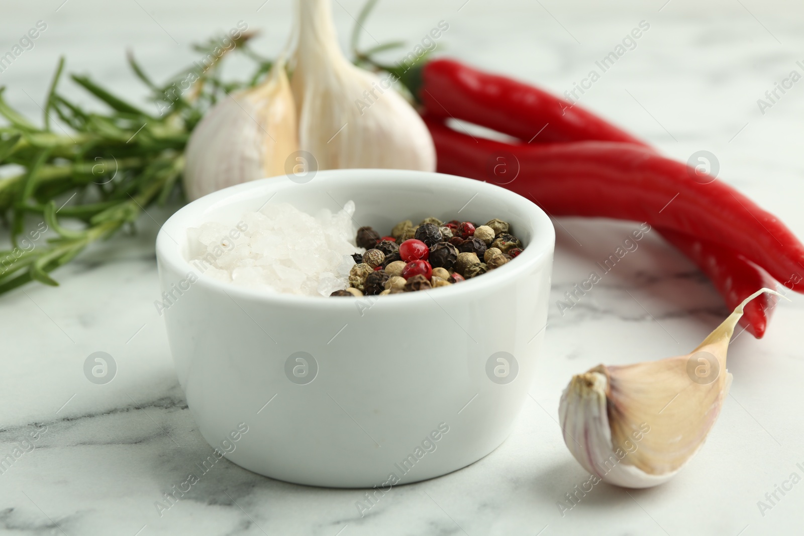 Photo of Sea salt, peppercorns, rosemary, chili peppers and garlic on white marble table, closeup