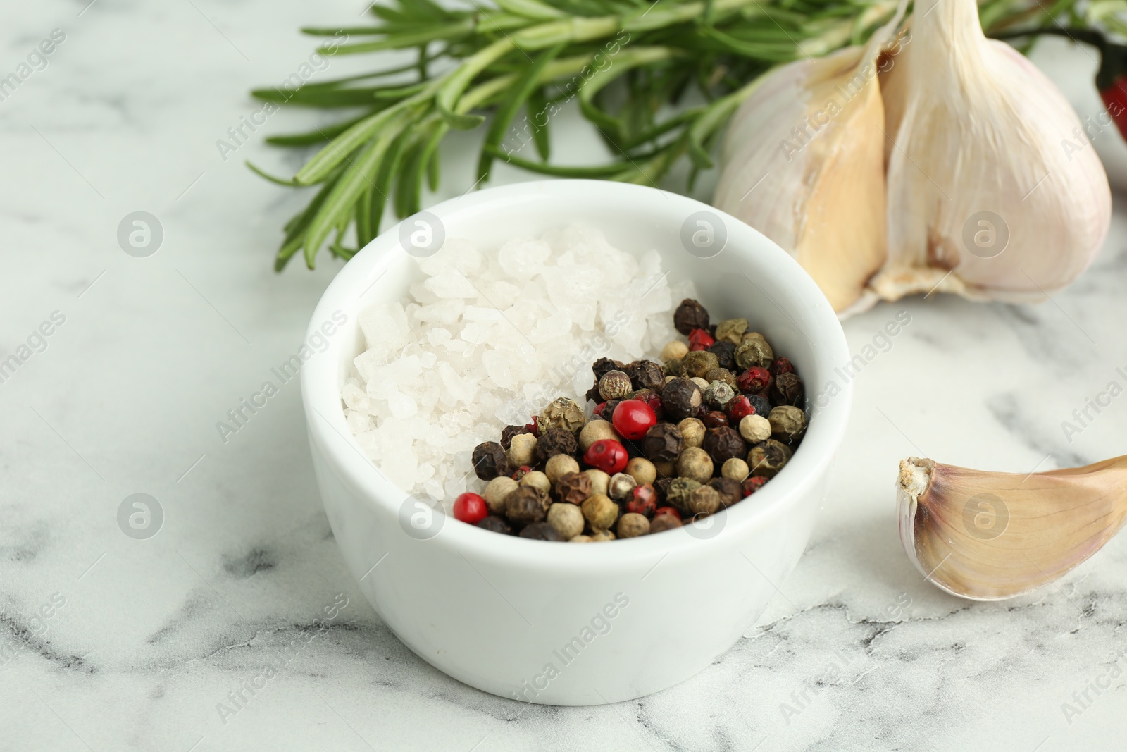 Photo of Sea salt, peppercorns, rosemary and garlic on white marble table, closeup