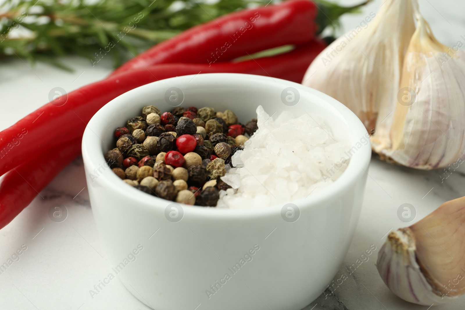 Photo of Sea salt, peppercorns, chili peppers and garlic on white marble table, closeup