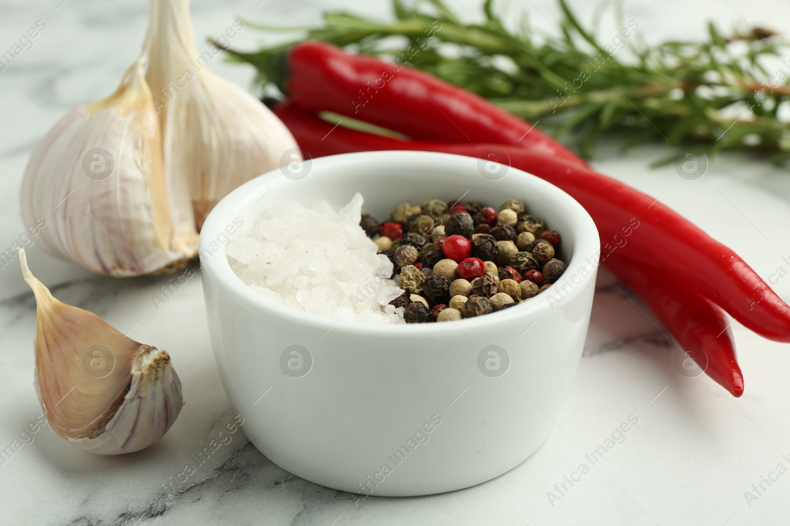 Photo of Sea salt, peppercorns, chili peppers and garlic on white marble table, closeup