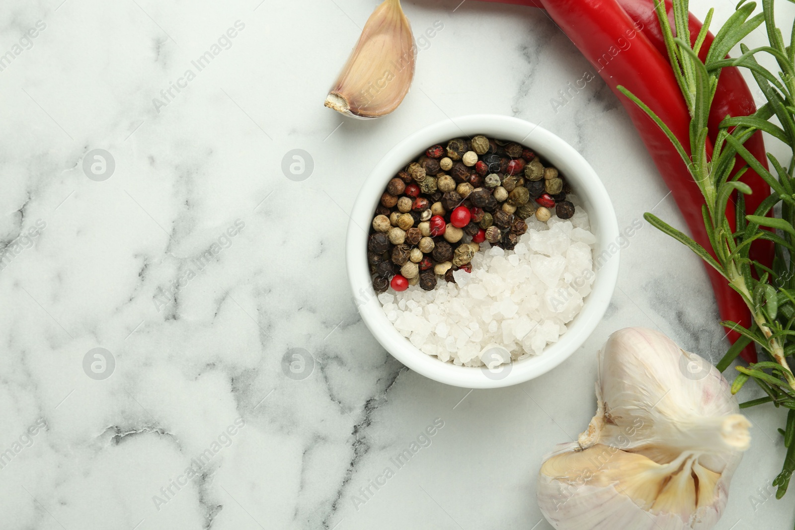 Photo of Sea salt, peppercorns, rosemary, chili peppers and garlic on white marble table, top view. Space for text