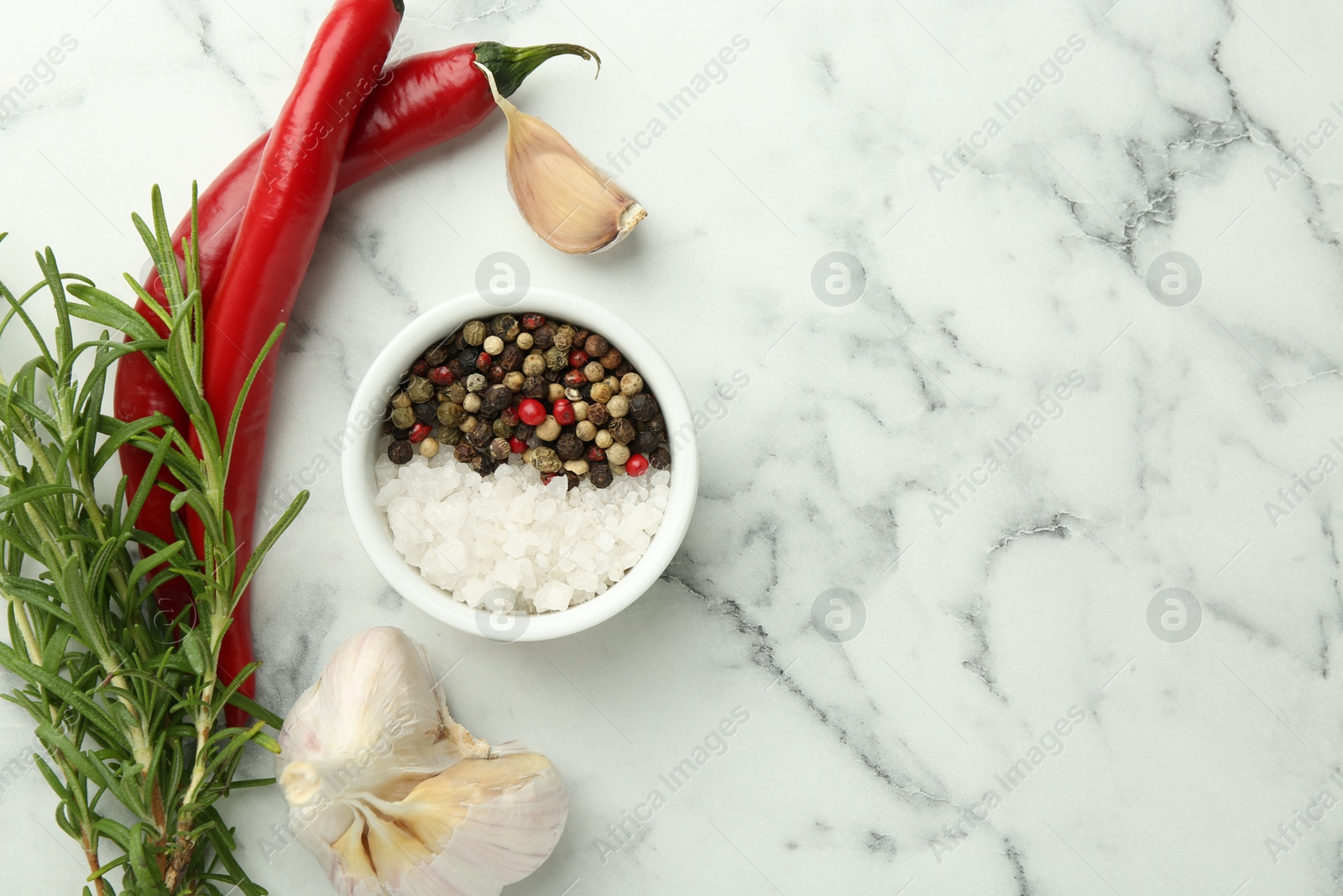 Photo of Sea salt, peppercorns, rosemary, chili peppers and garlic on white marble table, top view. Space for text