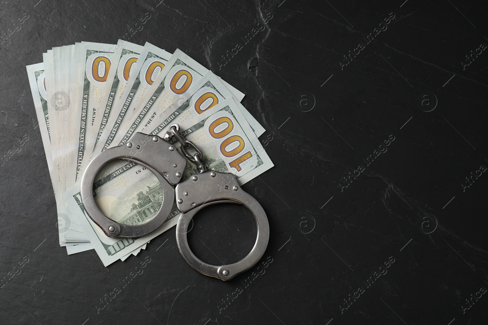 Photo of Corruption. Handcuffs and dollar banknotes on grey textured table, flat lay. Space for text