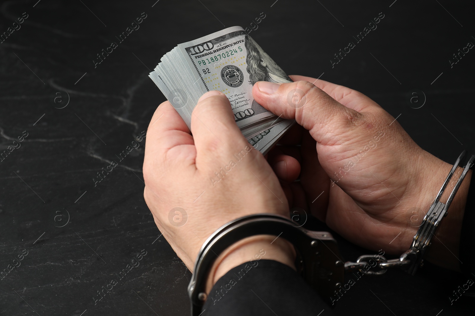 Photo of Corruption. Man in handcuffs holding dollar banknotes at grey textured table, closeup