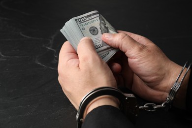 Corruption. Man in handcuffs holding dollar banknotes at grey textured table, closeup