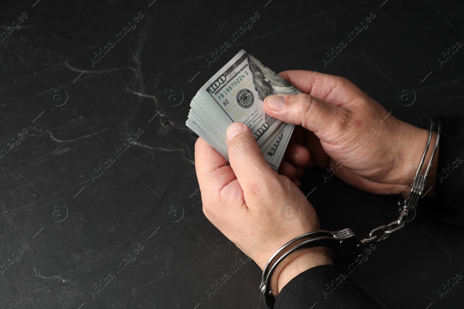 Photo of Corruption. Man in handcuffs holding dollar banknotes at grey textured table, closeup