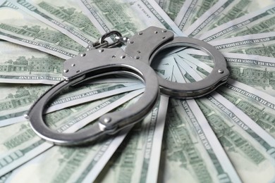 Photo of Corruption. Handcuffs on dollar banknotes, closeup view