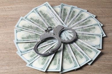 Photo of Corruption. Handcuffs and dollar banknotes on wooden table