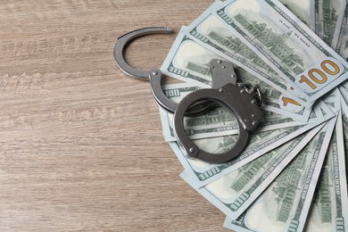 Photo of Corruption. Handcuffs and dollar banknotes on wooden table, space for text