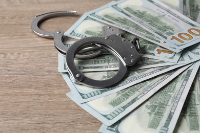 Photo of Corruption. Handcuffs and dollar banknotes on wooden table, closeup