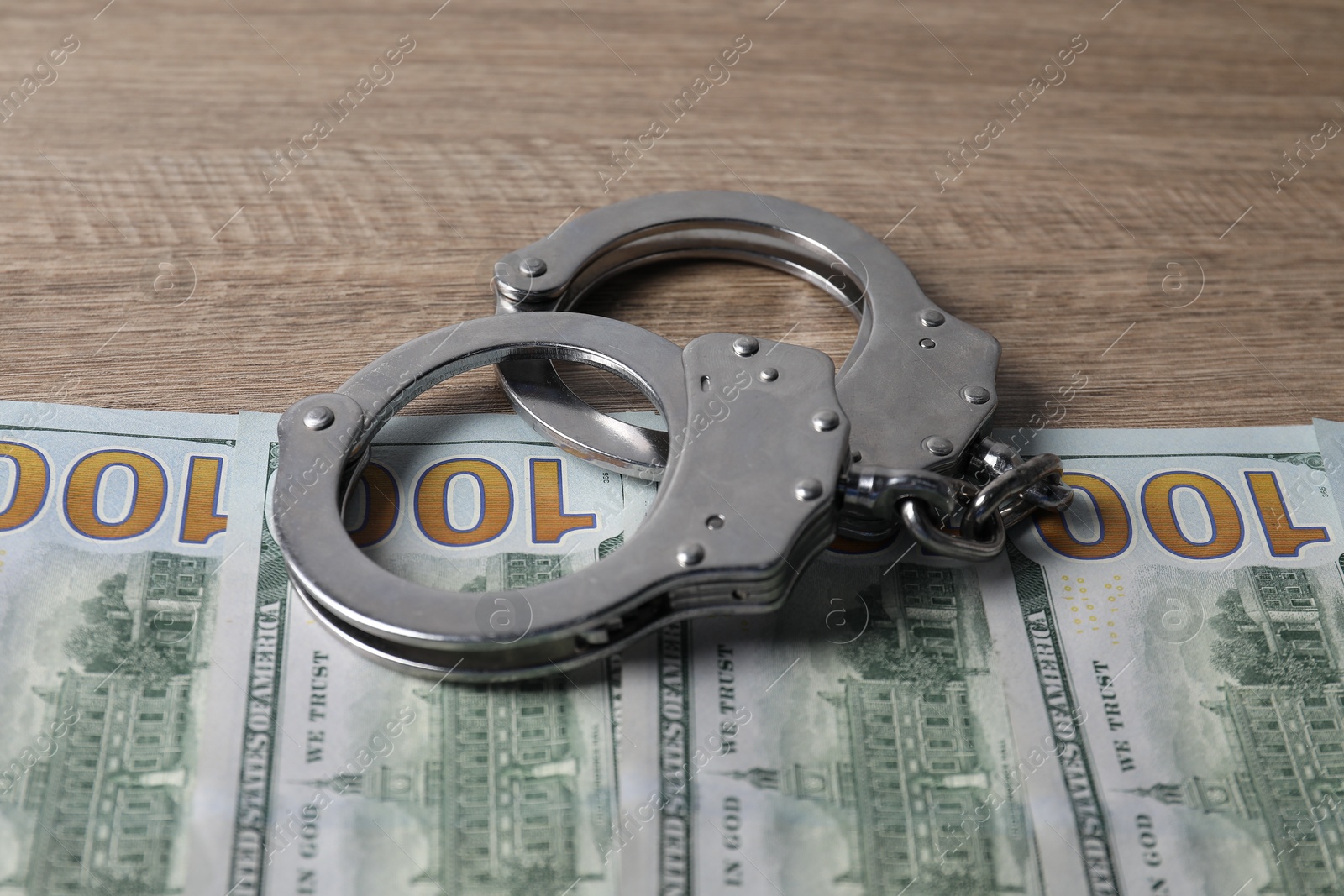 Photo of Corruption. Handcuffs and dollar banknotes on wooden table, closeup