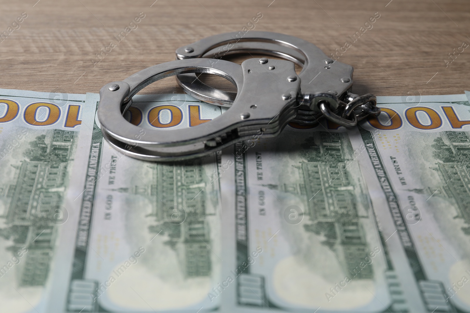 Photo of Corruption. Handcuffs and dollar banknotes on wooden table, closeup