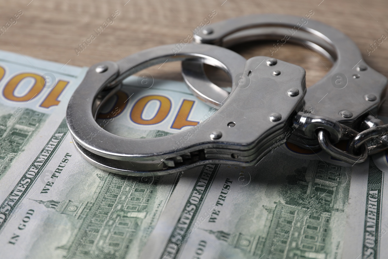 Photo of Corruption. Handcuffs and dollar banknotes on wooden table, closeup