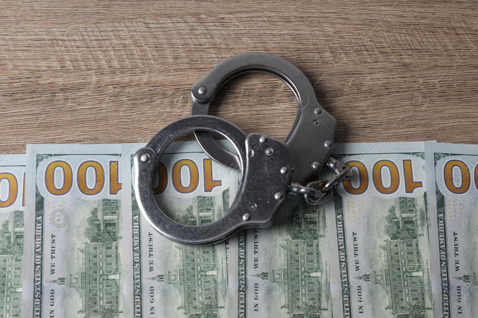 Photo of Corruption. Handcuffs and dollar banknotes on wooden table, flat lay