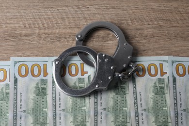 Photo of Corruption. Handcuffs and dollar banknotes on wooden table, flat lay