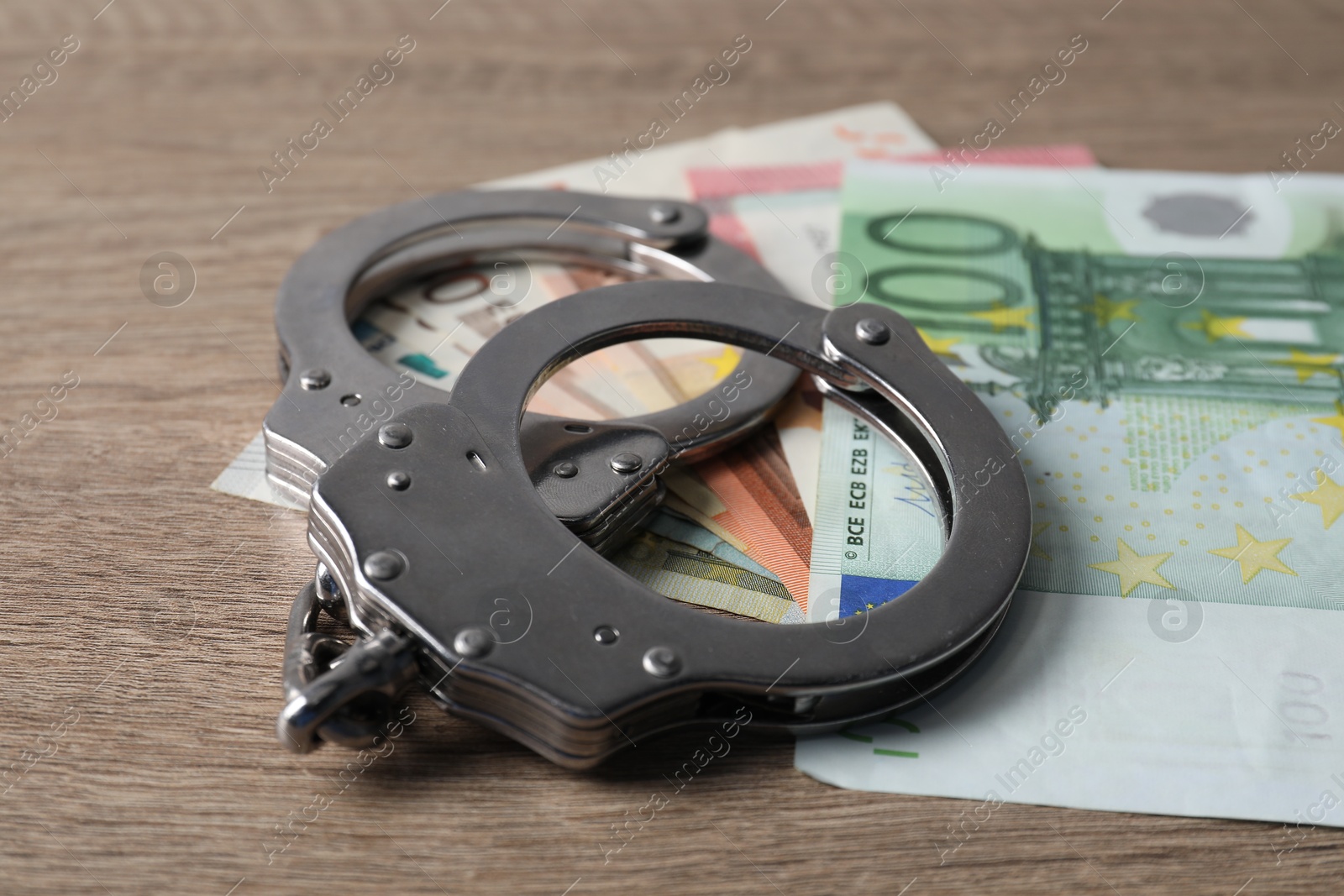 Photo of Corruption. Handcuffs and euro banknotes on wooden table, closeup